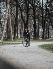 A boy rides his bicycle leisurely on a path in a city park, surrounded by nature and greenery.