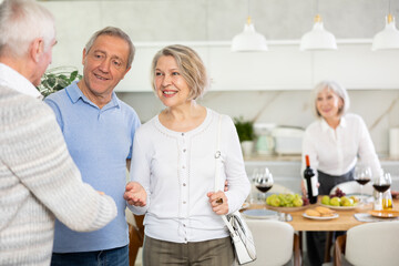 In cozy homely atmosphere, elderly male man shake hands with married couple, say goodbye after socializing and gatherings.