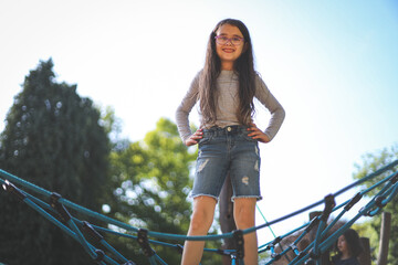 Obraz premium A caucasian girl of eight years old stands on a rope swing with a happy smile in the park