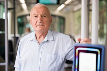 Elderly Caucasian man standing in tram and looking in camera.