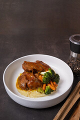 Plate of beef ribs in barbecue sauce with vegetables and mashed potatoes on dark background