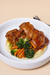 Close-up plate of beef ribs in barbecue sauce with vegetables and mashed potatoes angle view