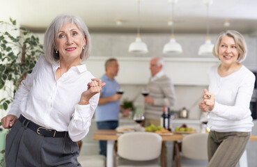 Elderly energetic woman dancing with friends in kitchen