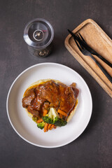 Plate of beef ribs in barbecue sauce with vegetables and mashed potatoes on dark background