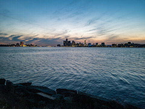 view of Downtown Detroit, Michigan and Downtown Windsor, Ontario skylines from sunset point in Belle Isle looking at the Detroit River at dusk with ambassador birdge visible partly cloudy evening