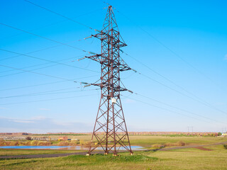 Metal power tower with high-voltage cables against the green field and the blue sky. The concept of energy, Energy transmission, the country's energy sector.