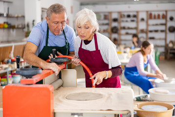 Elderly potter teaches a woman how to roll clay on a craft machine clay press roller