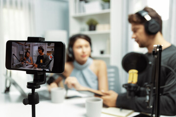 Fototapeta na wymiar Focus on smartphone recording with blurry host channel broadcasters background making advice problem in live streaming with listeners with set live on talking show radio at modern studio. Postulate.