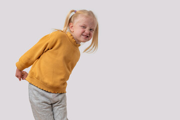Portrait of a little capricious girl in a yellow sweater on a white background