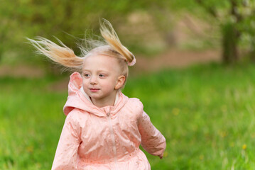 Portrait of jumping girl with two ponytails in pink outdoors jacket. European blonde girl 4-5 years...