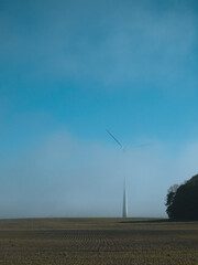 Wind turbine in the field covered with fog