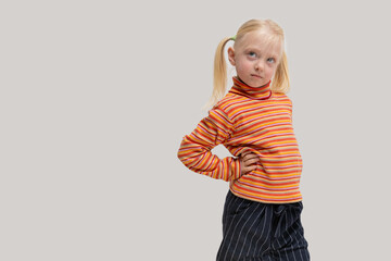 Portrait of a little girl with blond hair in an orange striped shirt and black trousers.