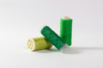 Close-up of spools of sewing thread in different shades of green on a white background.