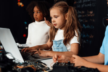 Smart girl in white bib learning about coding robotics technology using laptop in the STEM class....