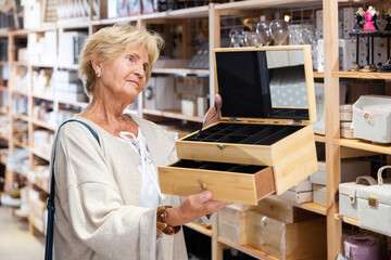 Positive elderly woman choosing jewelry storage container at store of household goods