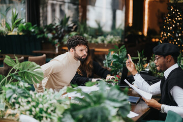 Three business colleagues casually reviewing documents at a cafe. They are surrounded by lush greenery and festive Christmas decorations.