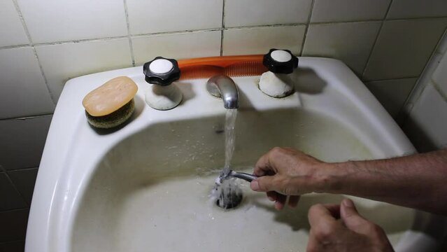 El hombre lava su maquinilla de afeitar despu&eacute;s de afeitarse en el antiguo ba&ntilde;o blanco, bajo agua corriente para limpiar la espuma de afeitar para el cuidado personal de rutina diaria