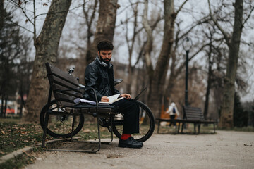 Stylish businessman focused on reading reports while seated on a bench in a tranquil park, exemplifying mobile work.