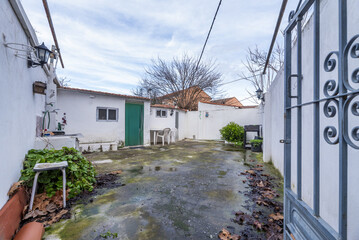 Interior patio of a house with cement floors with verdigris and rotting leaves, white painted walls and metal access door