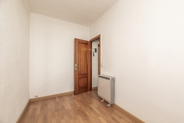 An empty room with light wooden floors and an electric heat accumulator next to the door