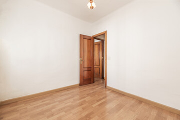 An empty room with white painted walls, wooden floor and sapelly door in a corner