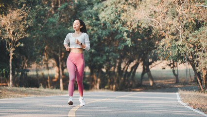 Full body female athlete in activewear running on road path during cardio workout on sunny summer day in park.