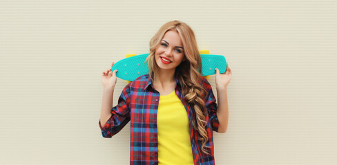 Stylish young blonde woman posing with skateboard on city street