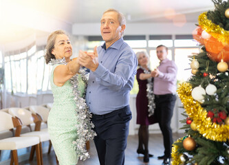Active mature men and women dancing samba dances in modern ballroom during celebration Christmas...
