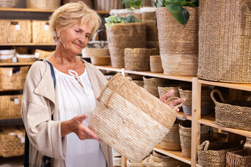 Fototapeta na wymiar Positive mature woman choosing wicker basket for a country house in hardware store