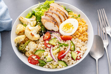Healthy lunch bowl with grilled chicken, roasted vegetables, fresh lettuce, cooked lentils, salad and boiled egg