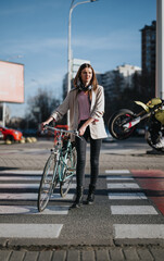 Obraz premium Confident young woman with a bike crossing the pedestrian lane in an urban setting against a blurred city background.