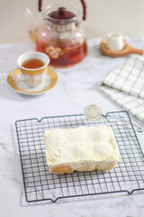 Milk Bun Thailand is a soft bread with a topping of powdered sugar, milk and vla filling, soft focus texture, served on black tray, napkin and vup of tea. white background. makanan viral indonesia
