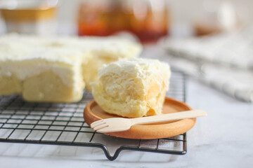 Milk Bun Thailand is a soft bread with a topping of powdered sugar, milk and vla filling, soft focus texture, served on black tray and cup of tea with a piece of milk bun. makanan viral indonesia