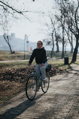 Naklejka premium Active adult female cyclist with a happy expression biking on a paved path in a scenic park, conveying a sense of freedom and happiness.