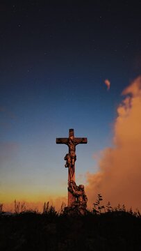 Beautiful clouds wrapped in red and yellow colors of the rays of the setting sun fly swiftly over the monument of the cross where Jesus was crucified. Vertical video.