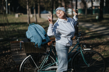 A cheerful young woman enjoys a sunny day in the park, playfully posing with a peace sign next to her vintage bicycle and backpack.