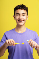 Handsome, smiling boy with braces holding toothbrush and toothpaste looking at camera