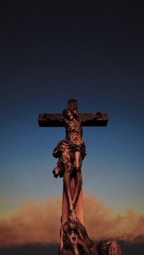 The monument of the cross on which Jesus was crucified, with Mary Magdalene next to it. During sunset, the clouds glow red-yellow, as if surrounded by fire.