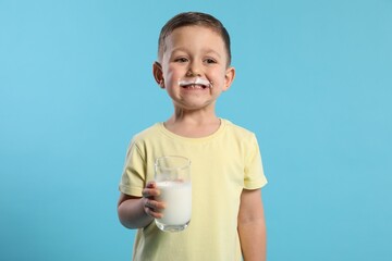 Cute boy with milk mustache holding glass of tasty dairy drink on light blue background