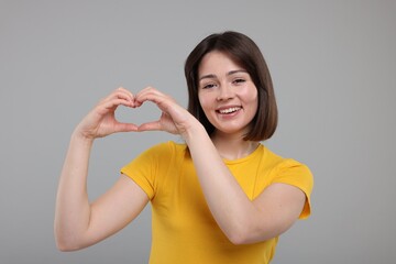 Happy woman showing heart gesture with hands on grey background