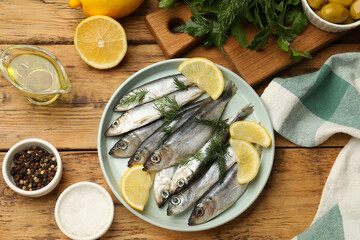 Fresh raw sprats, lemon and dill on wooden table, flat lay