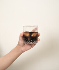 hand is holding a glass of coffee with ices on a white isolated background