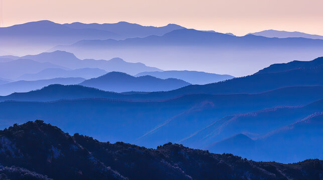 Layers of mountain ridges under a gradient twilight sky showcasing shades of blue purple and a hint of orange