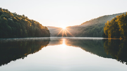 Serene lake at sunrise with calm water reflecting the sun nestled between gentle forestcovered hills - obrazy, fototapety, plakaty