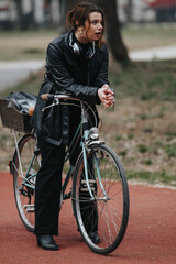 Confident and stylish young woman with headphones pausing during a bike ride in a city park, exuding elegance and determination.