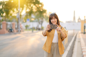 Traveler asian woman in her 30s using smartphone to take a photo while traveling urban street in Bangkok, Thailand