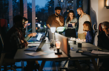 A mixed race team of multigenerational business colleagues engages in a meeting at a well-lit office during the evening hours, exemplifying teamwork.