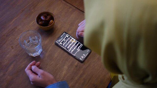 Woman hijab  reading the quran on the mobile phone in front of some dates and a glass of water in ramadan eid fitar i religious spiritual education islam muslim with hijab