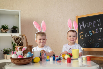 Two children with bunny ears funny painting Easter eggs at home