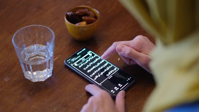 Woman hijab  reading the quran on the mobile phone in front of some dates and a glass of water in ramadan eid fitar i religious spiritual education islam muslim with hijab